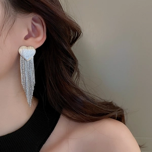 Detail of silver heart tassel earrings showing brushed metal texture on a female model