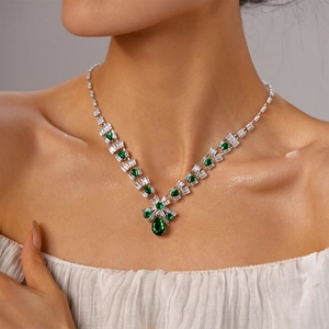 Detail view of a luxury zircon bow and emerald green teardrop necklace on model neck