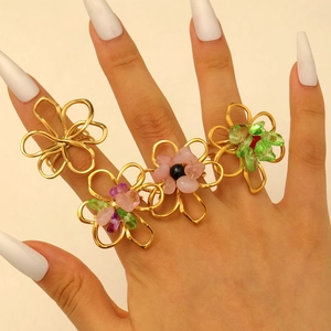 Detailed macro view of four golden hollow floral rings set with colorful beads on fingers