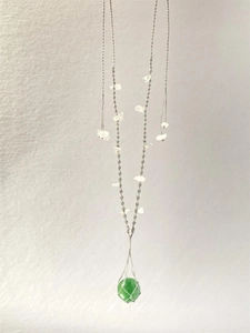 Détail d'un collier tissé main avec une pierre précieuse verte dans un filet gris