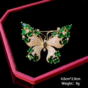 Detailed macro of a gold butterfly brooch with emerald gems and 4.0cm by 2.9cm dimensions
