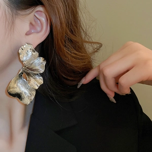 Close-up of oversized silver floral earrings with a brushed metal texture on a model