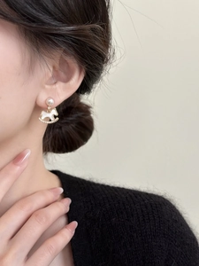 Macro close-up of a rocking horse stud earring with gold plating, pearls, and zircons