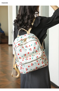 Detail view of white backpack with red cherry print and golden zippers worn by a model