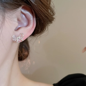 Close-up of a minimalist silver bow earring worn on a woman's ear with soft background