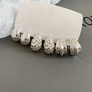 Close-up of three pairs of silver geometric stud earrings with smooth and hammered textures