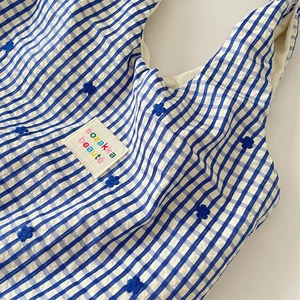 Détail du sac en toile à carreaux bleus avec fleurs brodées et étiquette tissée