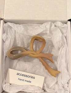 Macro view of gradient beige acrylic bow hair claw clip inside a white gift box