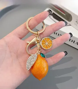 Macro detail of a bright orange lemon keychain with rhinestones and golden hardware