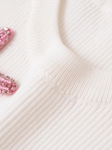 Close-up of white ribbed knit top featuring pink beads and rhinestone neckline details
