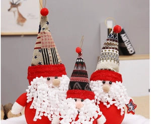Three plush Santa dolls with patterned hats on a soft snow-like base for holiday decor