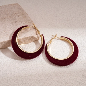Macro detail of 18K gold plated hoops wrapped in deep red velvet on a beige background