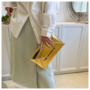 Detail of golden envelope clutch featuring crocodile pattern texture and metallic finish