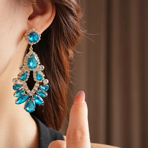 Close-up of gold dangle earrings with blue teardrop stones and rhinestones on model