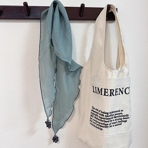 Off-white canvas tote bag with LIMERENCE text and grey-blue fringed scarf on a wall hook