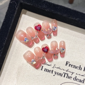 Detail of pink cat eye press-on nails with red heart gems and pearl decorations