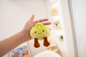 Close-up of cute steamed bun plush keychain with green body, long legs, and metal clasp