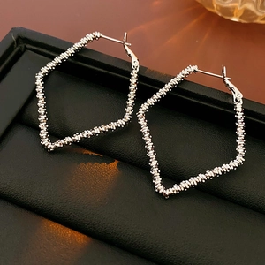Macro detail of silver rhombic earrings with woven metal texture in a black jewelry box