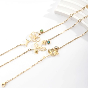 Three gold birthflower bracelets with colored gems on a white textured surface