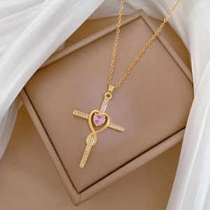 Macro view of gold cross pendant featuring a pink heart gem and pavé-set crystals