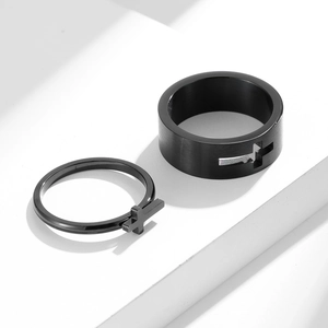 Detail of matte black stainless steel rings with cross cutout on white geometric base