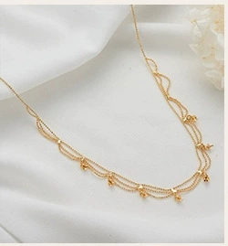 Detailed view of multilayer gold necklace with spherical pendants on white silk background