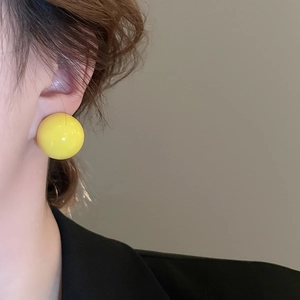 Macro side view of a large glossy yellow ball earring worn by a model in a minimalist style
