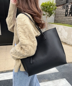 Detail of black pebbled leather tote bag with elegant tassel and large capacity