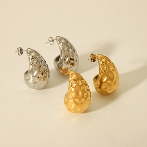 Macro detail of teardrop hammered earrings in gold and silver finish on beige background