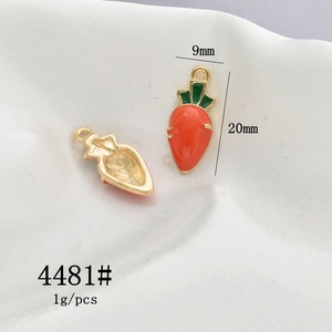 Detailed size view of two carrot charms with orange enamel and gold finish on white fabric