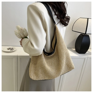 Detailed close-up of beige woven straw tote bag with black leather shoulder strap and texture