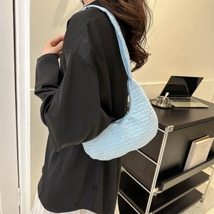 Minimalist light blue pleated crescent shoulder bag shown on model in home setting