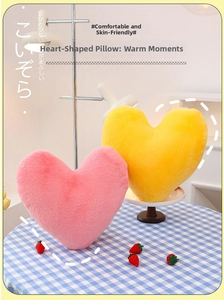 Pink and yellow heart-shaped plush pillows shown on a table in a cozy home setting