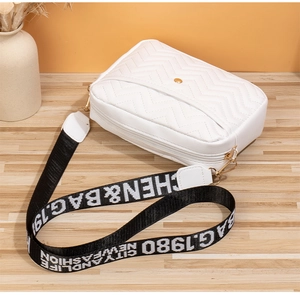 Detail of white quilted crossbody bag featuring wide letter-printed strap and metal hardware
