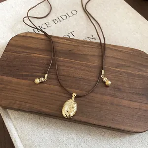 Elegant gold spiral oval pendant on brown wax cord necklace displayed on walnut tray
