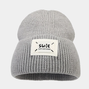 Close-up of grey knit beanie featuring a white square letter patch on the folded brim
