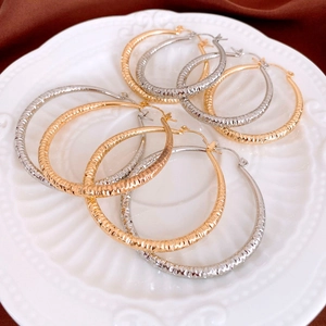 Detailed view of textured gold and silver hoop earrings with diamond-cut metal patterns