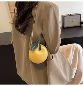 Detail of yellow round fruit shaped crossbody bag with green leaf and gold chain strap