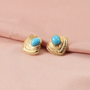 Golden heart-shaped hammered earrings with oval turquoise gemstones on pink fabric