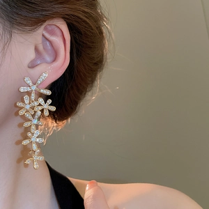 Close-up of long gold fringe earrings with crystal-encrusted five-petal flowers