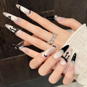 Faux ongles stiletto cat-eye style français avec nœuds noirs 3D et strass brillants