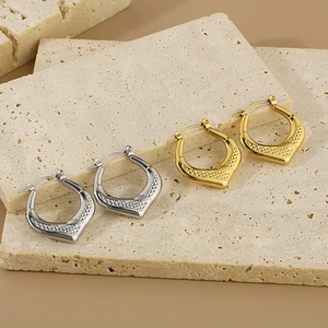 Detail of geometric shield earrings with diamond pattern texture on beige stone