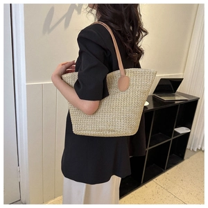Detail of hand-woven straw tote bag with brown leather shoulder straps in a modern setting