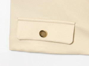 Gros plan sur la texture en sergé beige avec bouton en métal doré et détail de poche