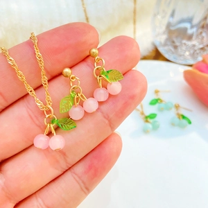 Dettaglio della collana con ciondolo a ciliegia rosa e orecchini a perno in una mano