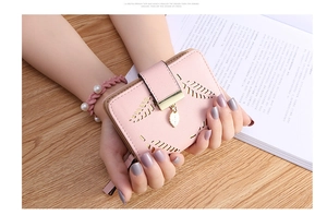 Close-up of pink short wallet with hollow leaf design and gold pendant in hand
