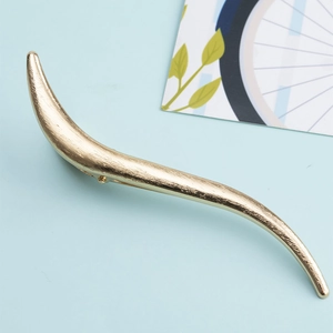 Macro detail of golden S-shaped metal hair clip with brushed texture on blue background
