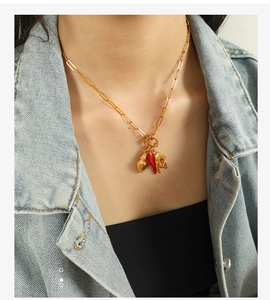 Detail of gold paperclip chain necklace with heart, chili pepper and figa hand charms