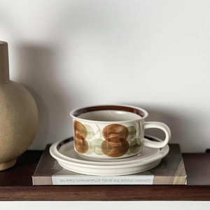 Close-up of vintage ceramic coffee cup with hand-painted floral pattern on a wooden shelf