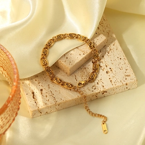 Macro detail of chunky gold chain bracelet on stone surface with elegant silk background